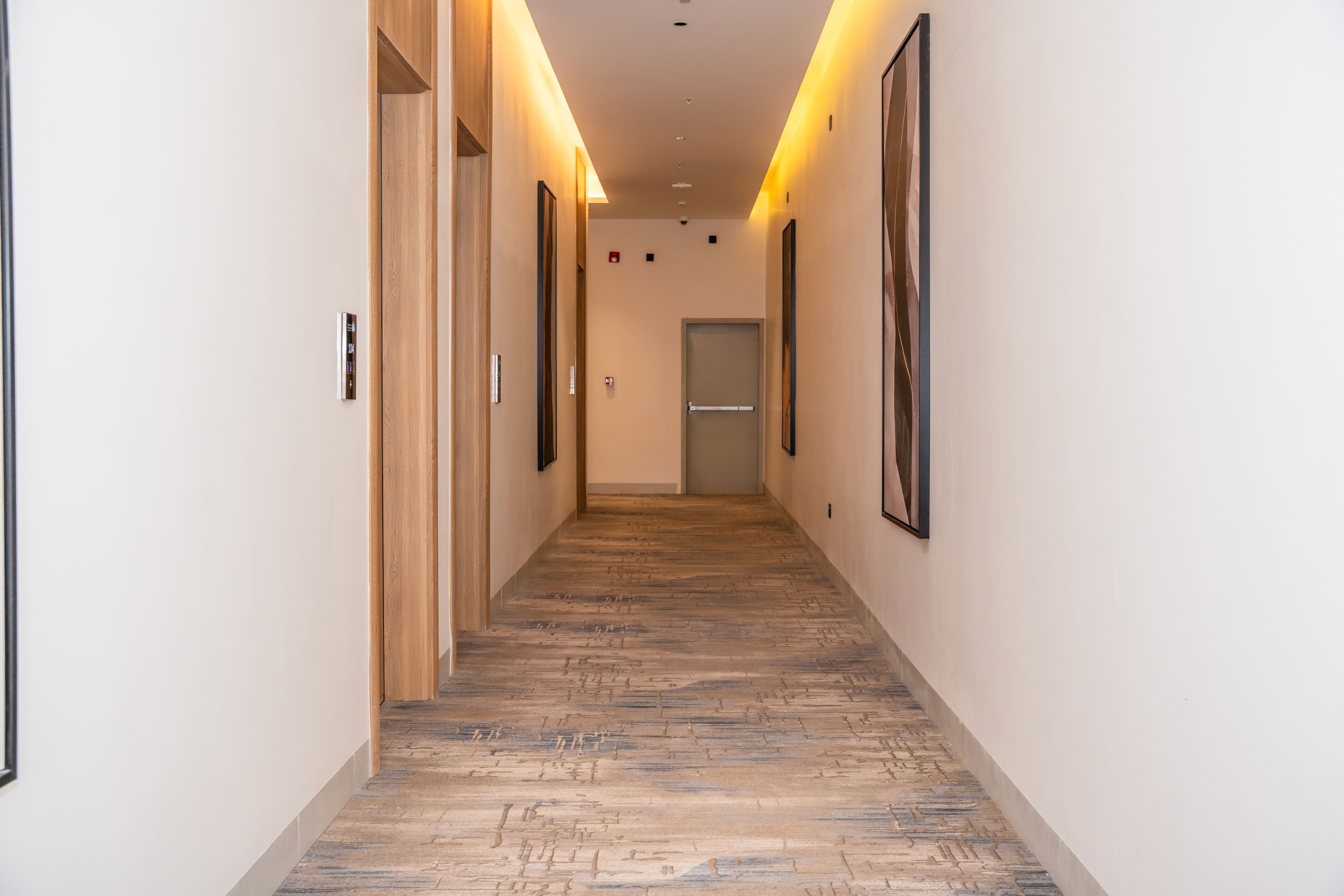 A hallway with a wooden floor, framed pictures on the walls, and a door at the end.