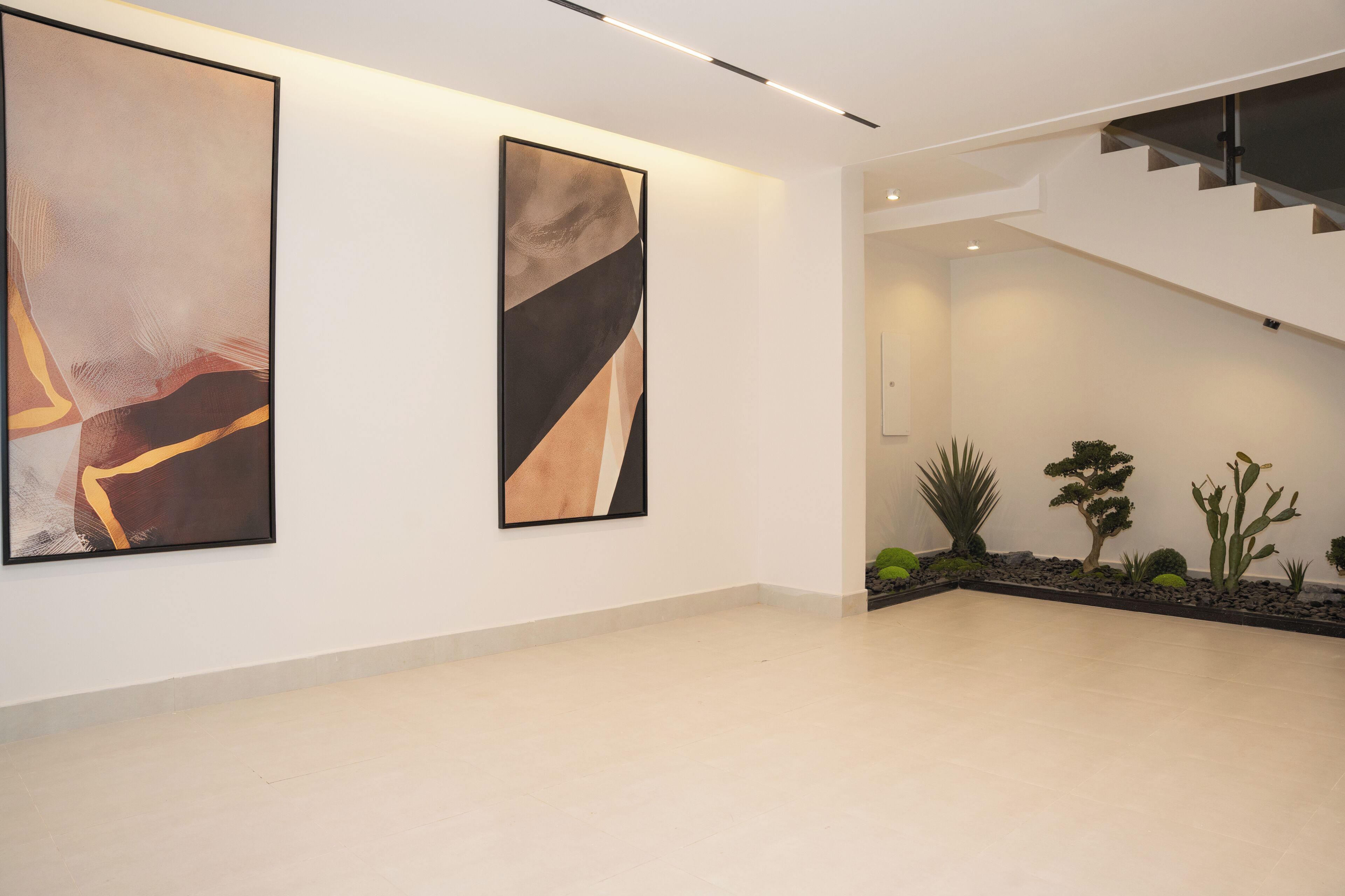 Un interior moderno con dos grandes cuadros abstractos en la pared, una escalera y un pequeño jardín interior con cactus.