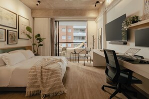 Ein modernes Hotelzimmer mit Bett, Schreibtisch, Stuhl, Fernseher und Blick auf ein Gebäude durch das Fenster.