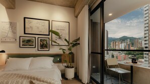 A hotel room with a bed, a potted plant, a balcony with a table and chairs, and city views. - Studio Nomad Pro | A/C, just steps from the Metro (Sabaneta)