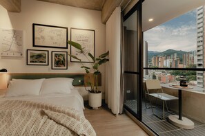 Ein Hotelzimmer mit Bett, einer Zimmerpflanze, einem Balkon mit Tisch und Stühlen sowie Blick auf die Stadt.