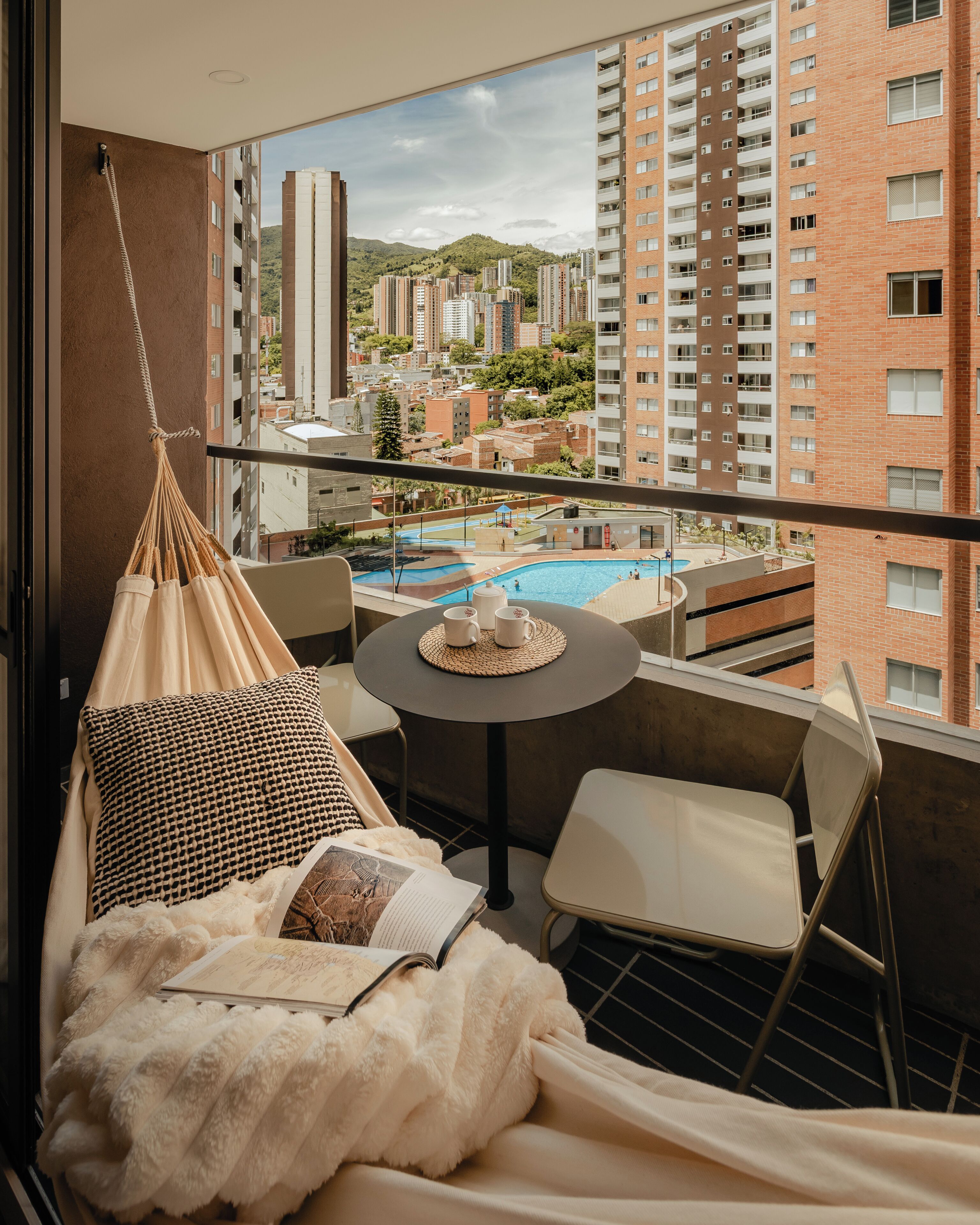 A balcony with a hanging chair, a small table with a cup and saucer, and a book.
