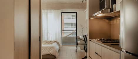 A modern kitchen with a built-in refrigerator, a dining area with a chair, and a bedroom with a bed.