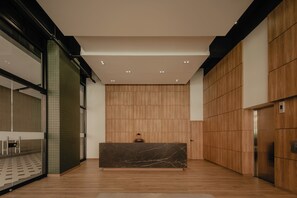 Ein moderner Empfangsbereich mit Marmor-Rezeptionstresen, Holzwandverkleidungen und einer Glastrennwand links.