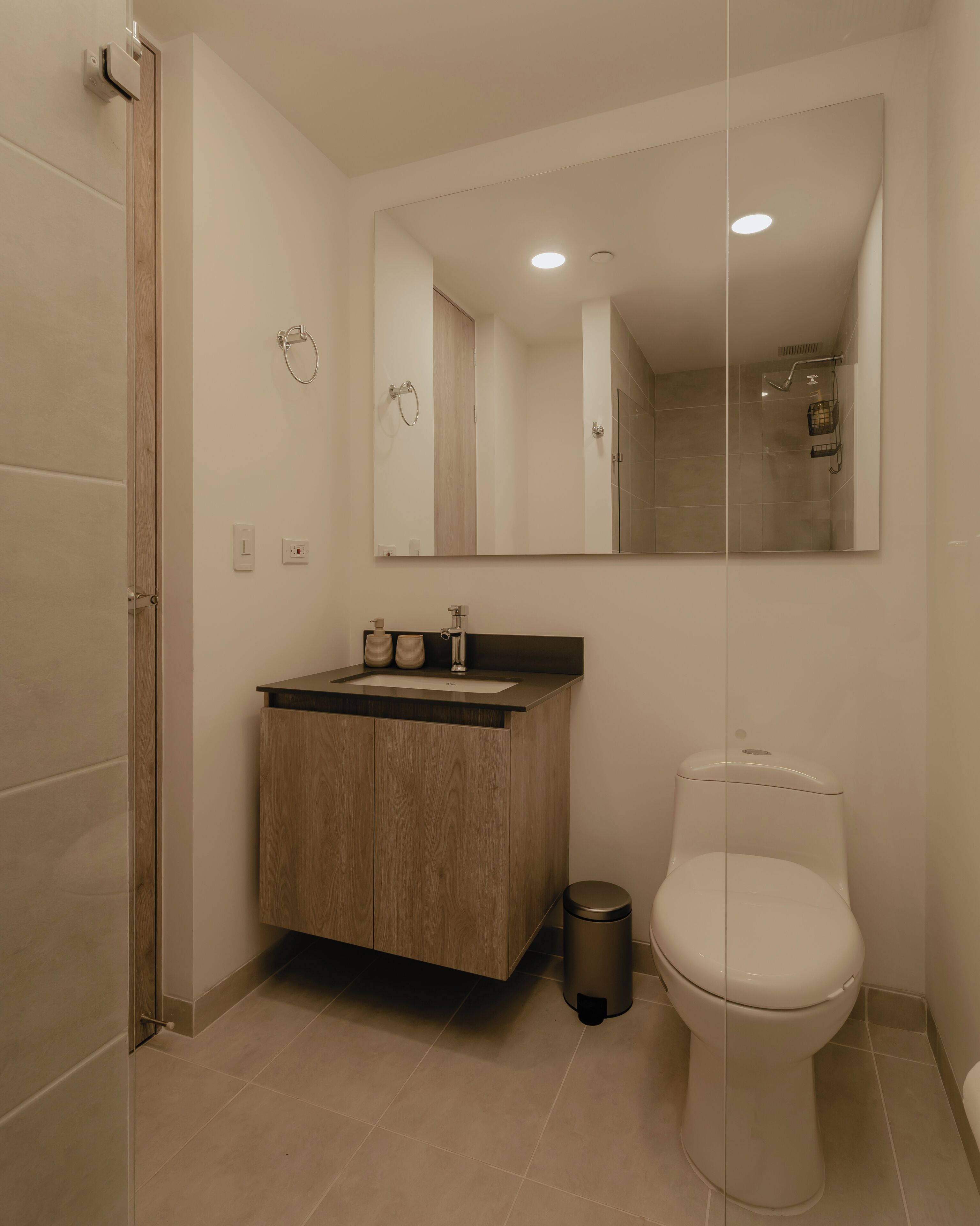 A modern bathroom with a wooden vanity, a toilet, and a glass shower enclosure.