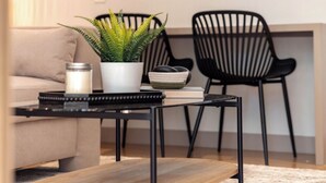 A modern living room with a sofa, a coffee table, a potted plant, a candle, and two black chairs. - Live in Provenza Modern 1 BR Security (Medellín)