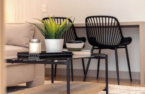 A modern living room with a sofa, a coffee table, a potted plant, a candle, and two black chairs. - Live in Provenza Modern 1 BR Security (Medellín)