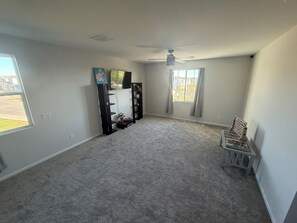 A room with a carpeted floor, a ceiling fan, a TV on a stand, and a window with curtains. - Charming  4BR/3B home with pool access near Superstition Mountains (Apache Junction)