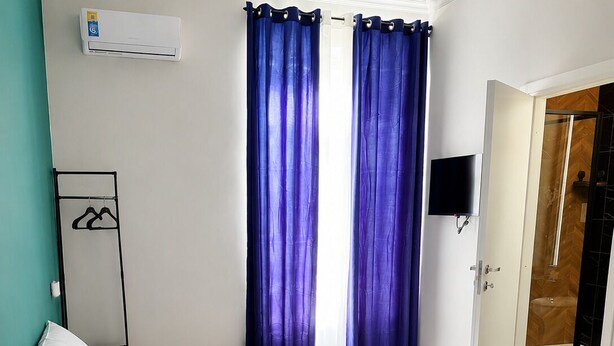 A hotel room with a bed, a TV, an air conditioning unit, and a wardrobe.