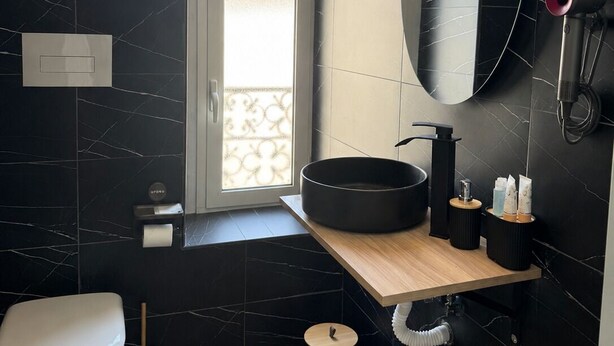 A modern bathroom with a black marble wall, a round sink, a toilet, and a window with a view. - Pisacane Family's Rooms (Naples)