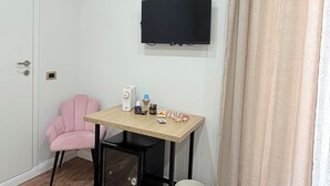A room with a wooden desk, a pink chair, a television mounted on the wall, an air conditioner, and a curtain.