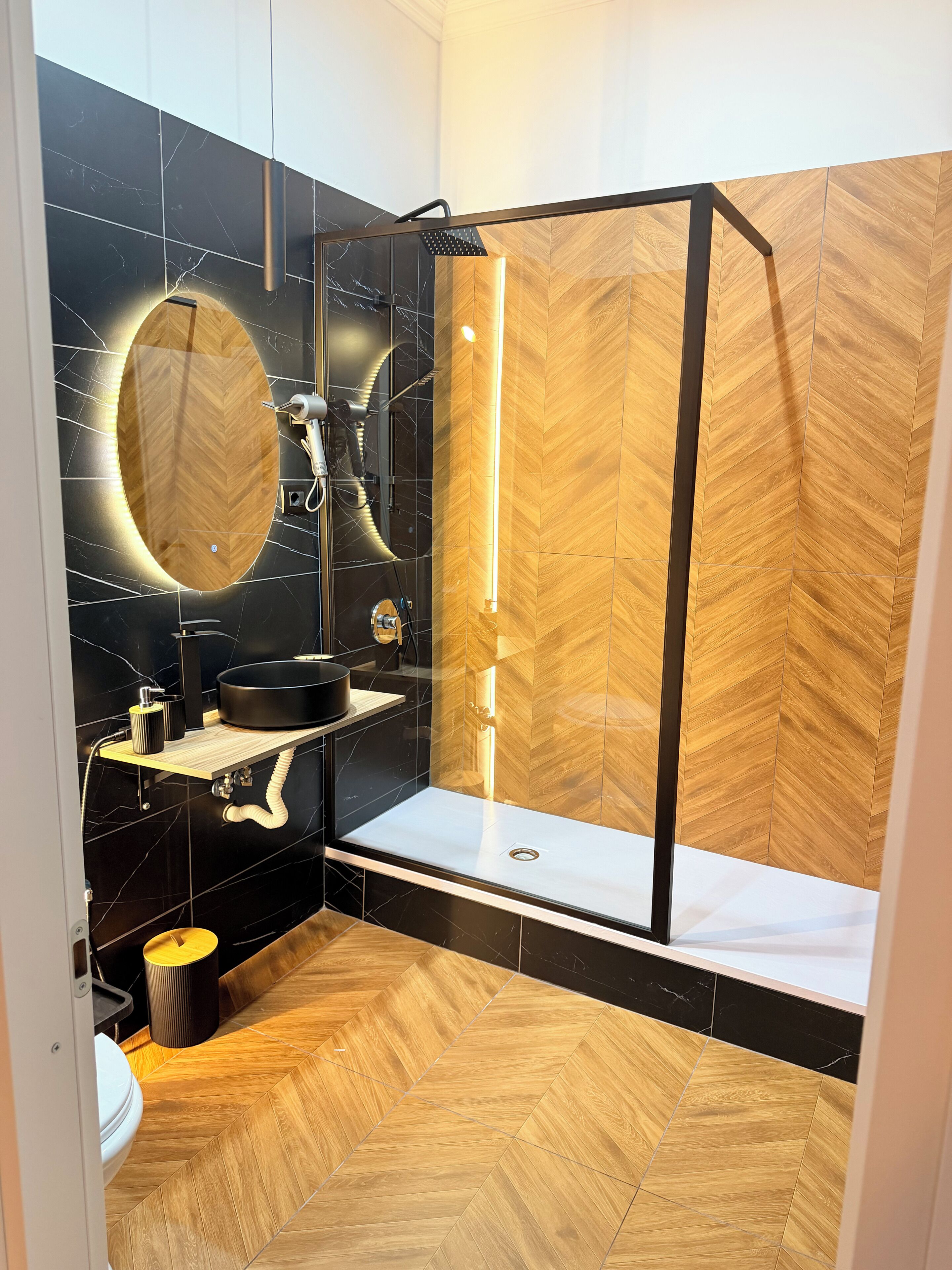 A modern bathroom with a shower enclosure, a vanity with a mirror, and a herringbone-patterned floor.