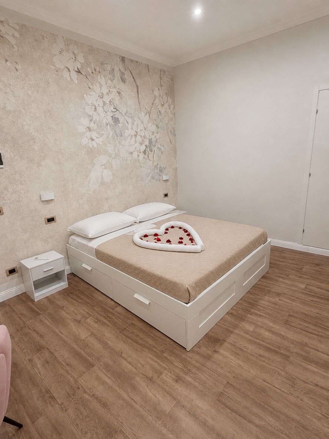 A bedroom with a bed, a nightstand, a dresser, and a wall with a floral pattern.