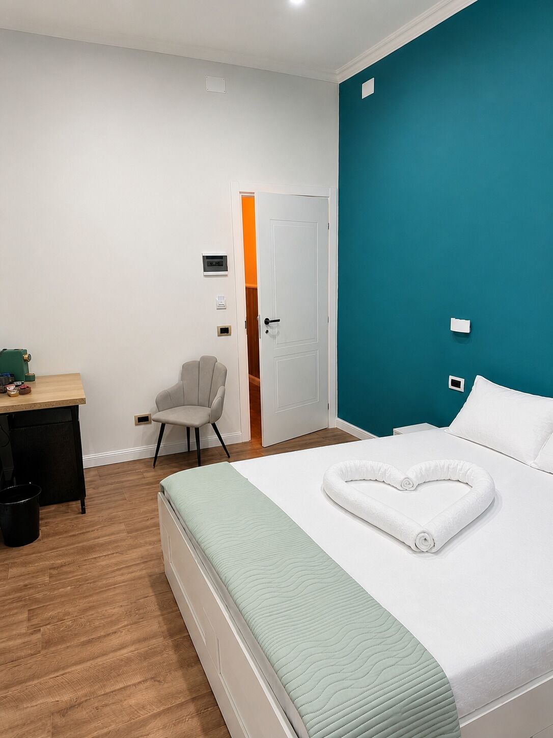 Ett hotellrum med en säng, ett skrivbord, en stol och en dörr som leder till ett annat rum.