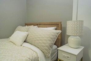 A bed with a wooden headboard, a bedside lamp with a patterned lampshade, and a white nightstand with a power outlet. - Quiet neighbourhoo
Family friendly
Edmonton Expo Centre
Convenient & comfortable (Edmonton)