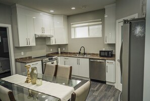 A modern kitchen with white cabinets, a stainless steel refrigerator, a microwave, and a dining area with a glass table. - Quiet neighbourhoo
Family friendly
Edmonton Expo Centre
Convenient & comfortable (Edmonton)