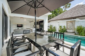 A modern outdoor dining area with a pool, a Buddha statue, and a kitchen visible in the background. - Shala Suites Bali - Pererenan (Mengwi)