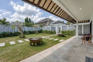 Een modern buitenterras met een pad van stenen, een fontein in het midden en een zithoek met stoelen.