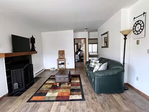 Ein Wohnzimmer mit Kamin, einem grünen Sofa, einem gemusterten Teppich und einem Fernseher auf einem Holzboden.