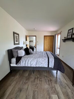 Ein Schlafzimmer mit einem Bett, Holzboden, einer Tür und einem Fenster.