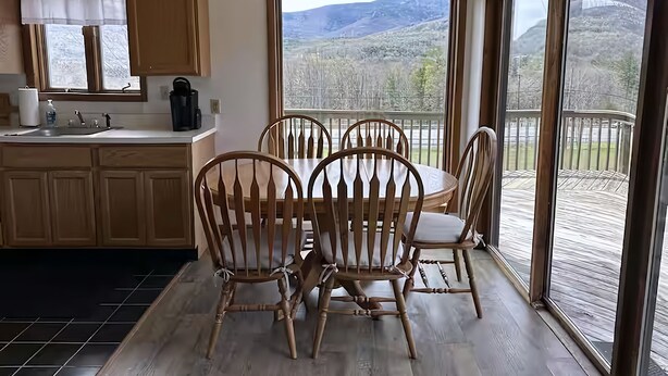 A dining area with a table and chairs, a kitchen with a coffee maker, and a view of a snowy landscape through large windows. - Vacation Home. 4 Minutes to Hunter Mountain! (Hunter)
