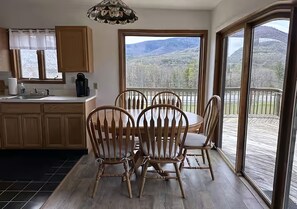 A dining area with a table and chairs, a kitchen with a coffee maker, and a view of a snowy landscape through large windows. - Vacation Home. 4 Minutes to Hunter Mountain! (Hunter)