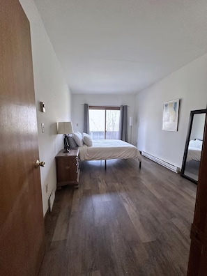 A bedroom with a bed, bedside table, lamp, and a view through a window. - Vacation Home. 4 Minutes to Hunter Mountain! (Hunter)