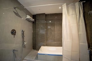 A modern bathroom with a bathtub, shower, and a ceiling-mounted air conditioning unit. - Hotel Shivalik (Mehsana)