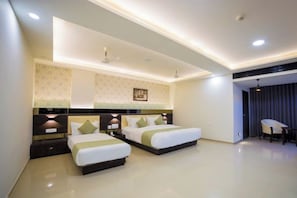 A hotel room with two beds, a desk, and a chair. - Hotel Shivalik (Mehsana)