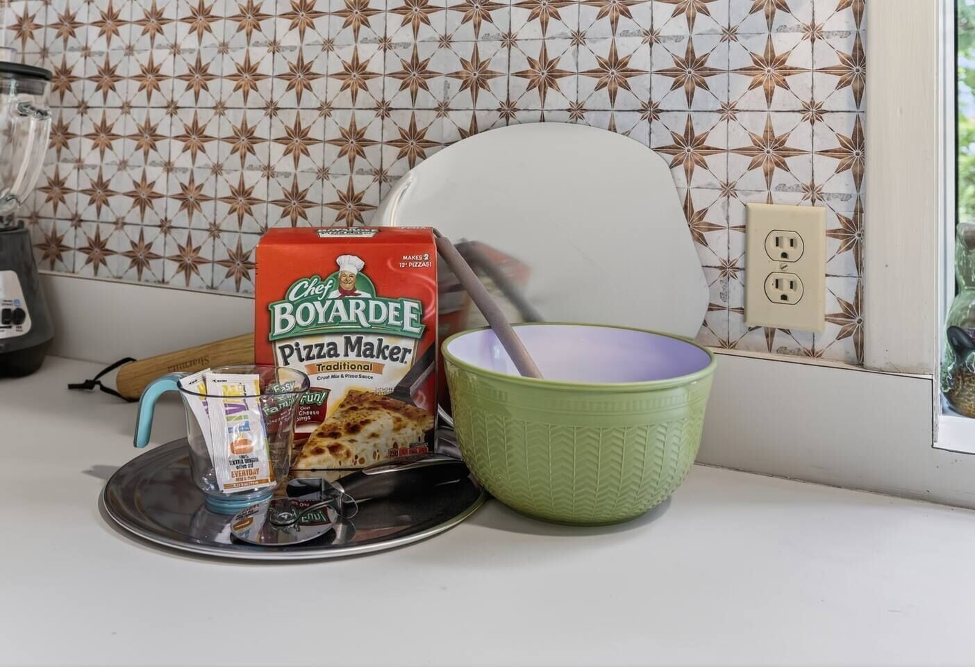 A kitchen counter with a pizza maker, a green bowl, and a pizza box.