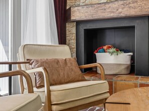 Un coin salon accueillant avec un fauteuil confortable, une petite table ronde et une cheminée agrémentée d’un panier tressé rempli de fleurs.