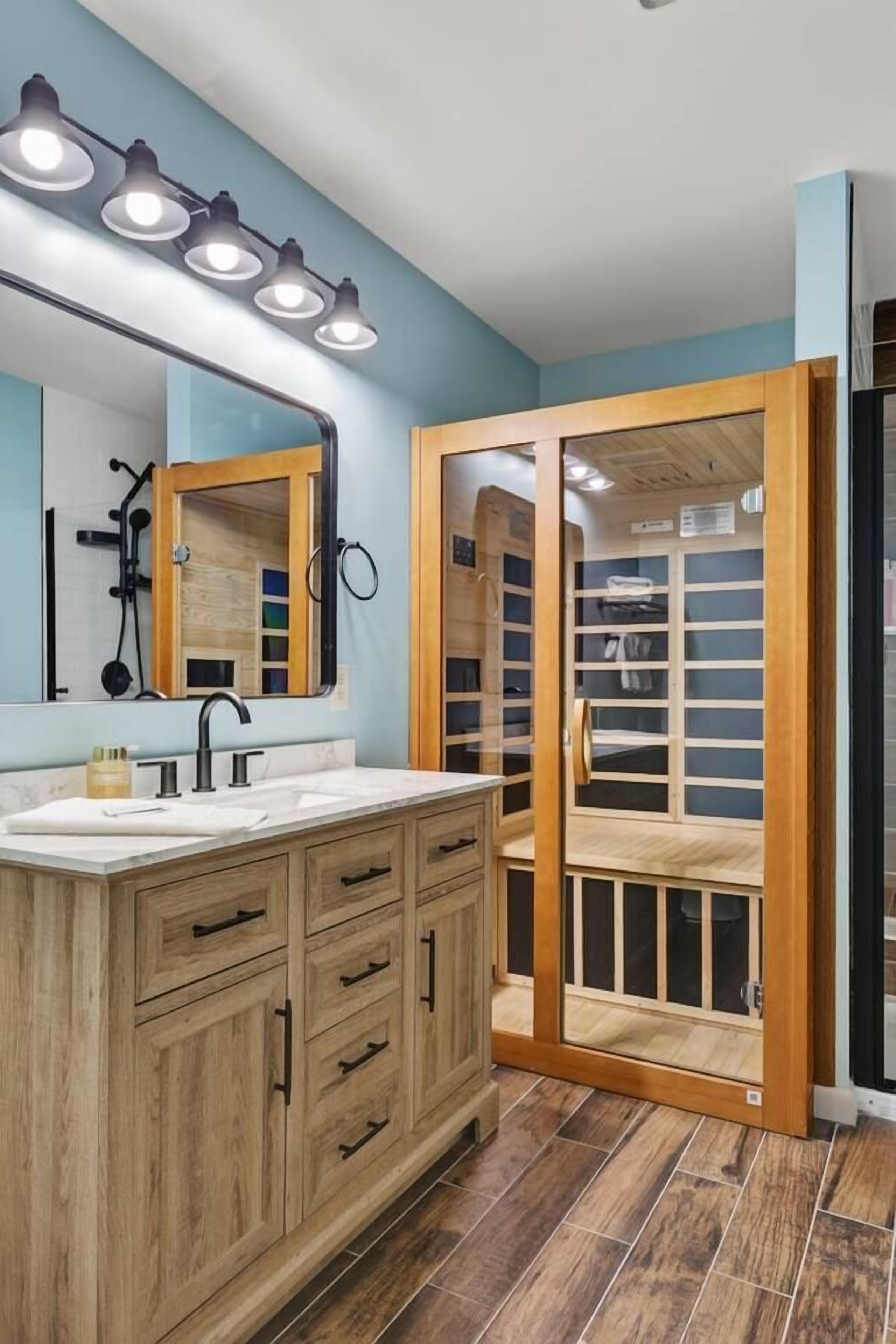 Un bagno con un mobiletto vanità in legno, uno specchio grande e uno spazio doccia.