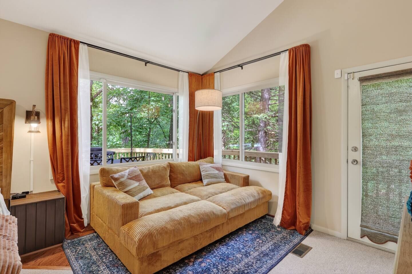 A cozy room with a large window, a sofa, and a lamp.