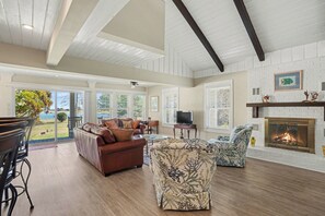 A spacious living room with a fireplace, leather sofas, and a view of a lake. - Peaceful 4-bedroom cottage in Oyster Bay Golf Community (Sunset Beach)