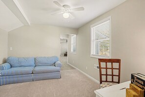 A room with a ceiling fan, a striped sofa, a wooden chair, and a window with blinds. - Peaceful 4-bedroom cottage in Oyster Bay Golf Community (Sunset Beach)