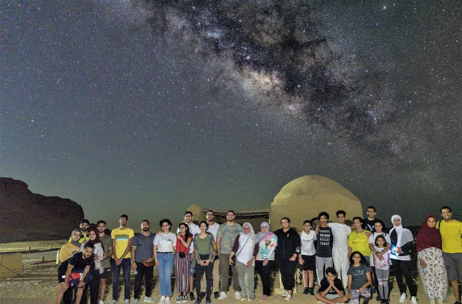 A group of people posing in front of a large rock formation under a starry night sky.