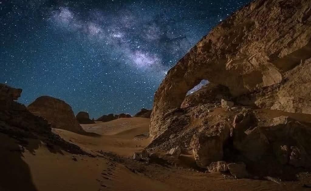 Un paysage désertique avec une arche rocheuse imposante se détachant sur un ciel étoilé.