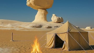A desert campsite with a large rock formation, a fire, and a tent.