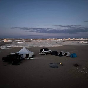 Un camping con tiendas de campaña, un vehículo y un paisaje rocoso.
