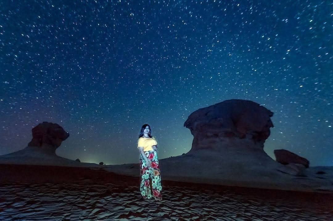 A person standing in a desert with a starry sky.