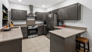 A modern kitchen with dark cabinetry, stainless steel appliances, and a marble countertop.
