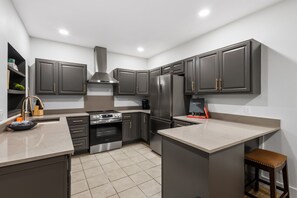 A modern kitchen with dark cabinetry, stainless steel appliances, and a marble countertop.