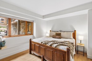 Un dormitorio con cama de madera, pared de piedra, ventana y mesita de noche.