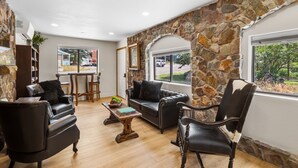 A living room with stone walls, leather furniture, a coffee table, and a view of the outside.