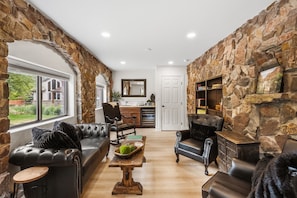 A living room with stone walls, leather sofas, a wooden coffee table, and a view of the outside.