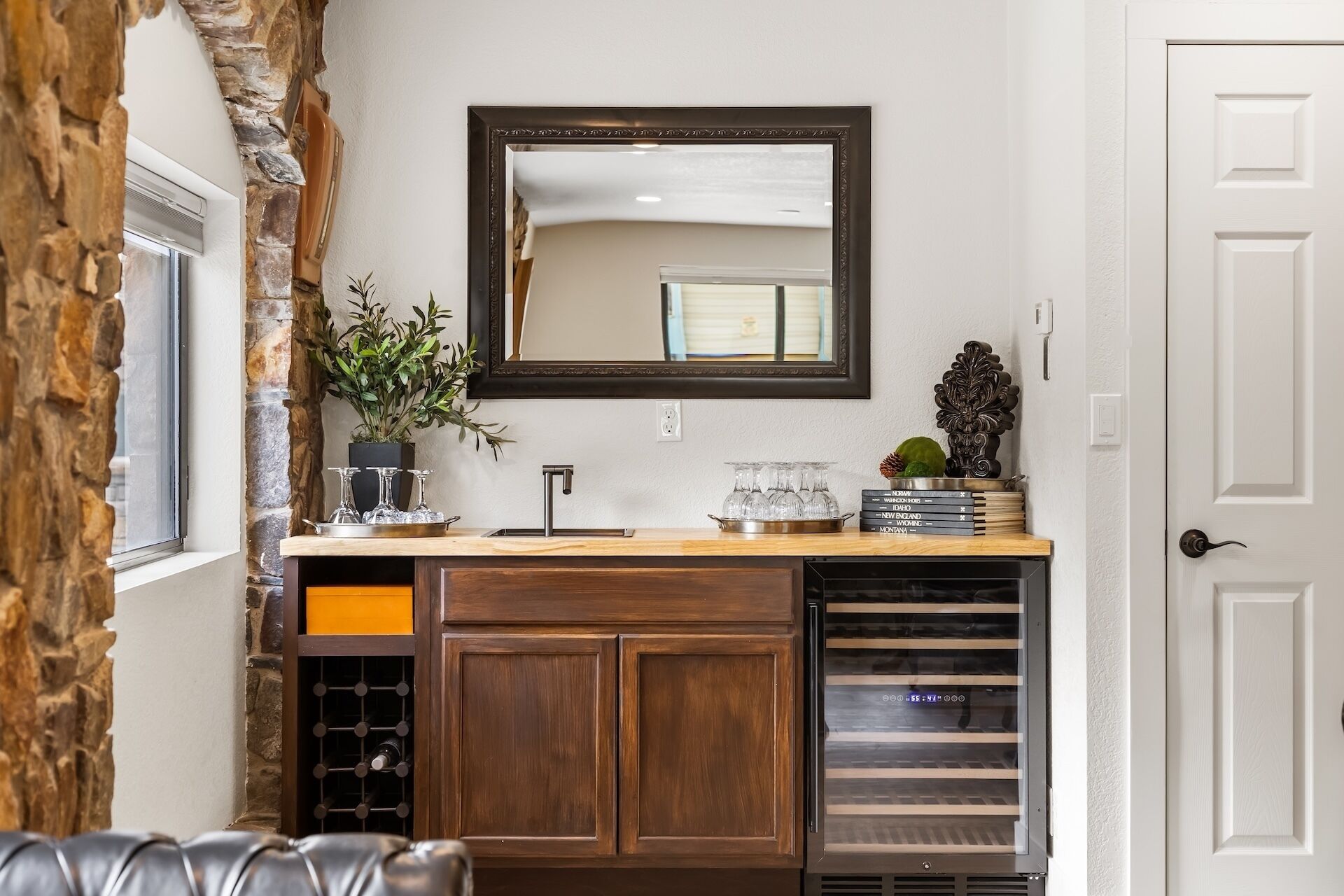 A kitchen with a stone accent wall, a wooden cabinet, a wine rack, and a mirror above the counter.