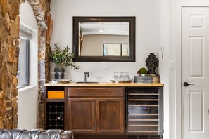 A kitchen with a stone accent wall, a wooden cabinet, a wine rack, and a mirror above the counter.