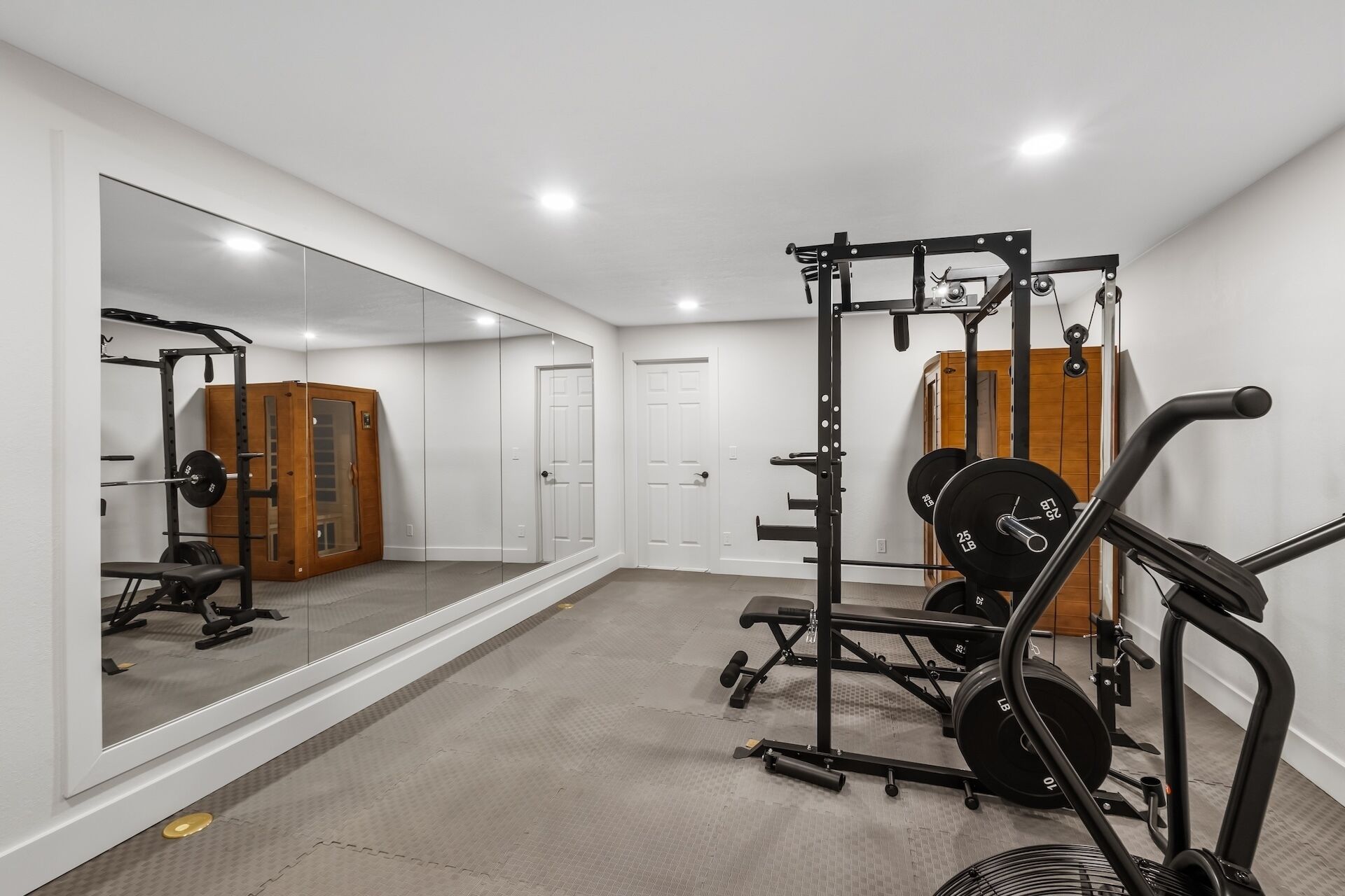 A home gym with a mirrored wall, weightlifting equipment, and a door.