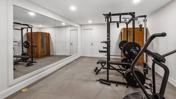 A home gym with a mirrored wall, weightlifting equipment, and a door.