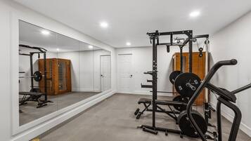 A home gym with a mirrored wall, weightlifting equipment, and a door.